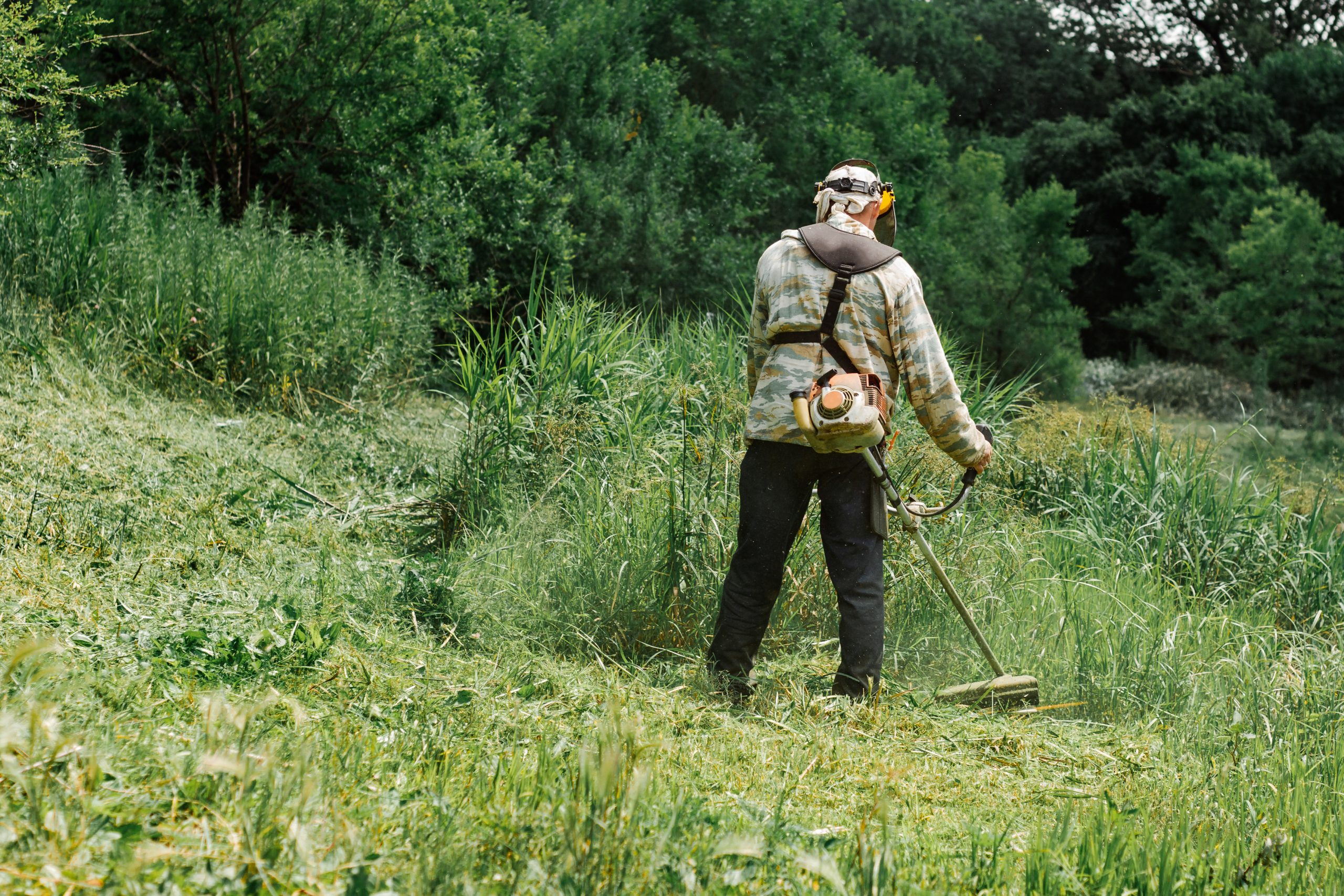A working man mowing the tall grass with a lawn mower